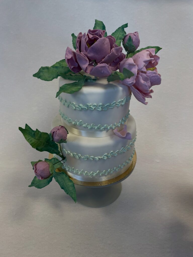 Bröllopstårta med lila pioner och gröna blad i sockerpasta